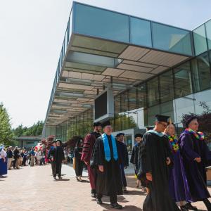Faculty and staff walking past Carver Gym on sunny day during Commencement